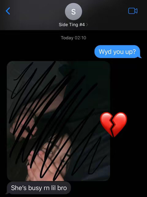The image showcases a simulated phone text message conversation. The background is black. There are two chat bubbles: one on the right says "Wyd you up?" in a light blue bubble. The other, a light grey bubble at the bottom, reads "She's busy rn lil bro." Inside, a picture of two intertwined figures is heavily obscured by black scribble marks. A broken heart emoji is placed on the upper right.