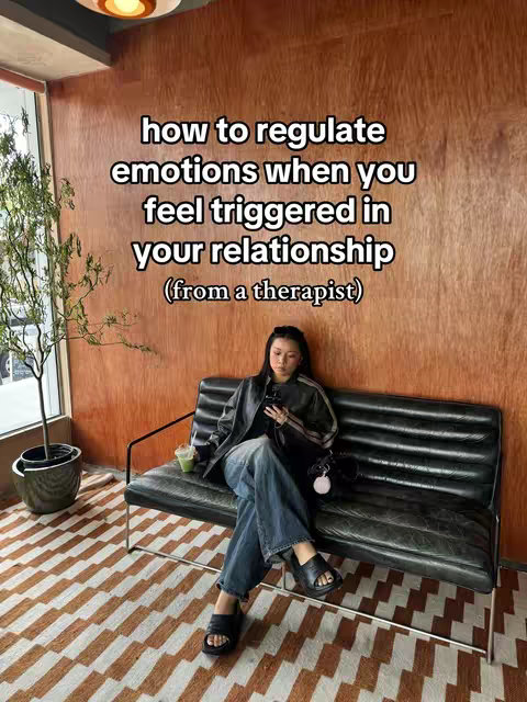 A person is seated on a black leather bench with a black jacket and blue jeans, holding a phone. Text overlayed on the image reads,  how to regulate emotions when you feel triggered in your relationship (from a therapist)