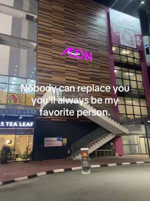 A nighttime shot of a commercial building with a large neon sign that reads "AEON." The building has a facade with a horizontal pattern of brown and tan rectangles. In front of the building is a black staircase with white stairs leading up to a door. The hook text is overlaid on the bottom of the image, over a Tea Leaf sign.