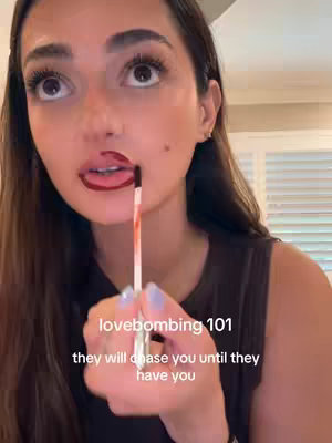 A close-up shot of a woman applying lipstick, with a text overlay describing lovebombing.