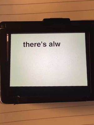 A digital display screen showing the phrase "there's alw" in a plain font, set against a light background. The screen is set within a black device, likely a tablet or similar gadget. The background consists of light-colored, lined paper, with the device resting on top of it.