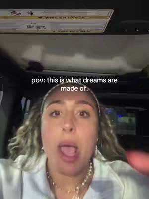 A selfie shot taken from inside a vehicle, likely a car. The creator, a woman, is the central focus with her face filling much of the frame. She has light skin, curly blonde hair, and is wearing a white top and a decorative beaded necklace. Text overlayed on the image reads 'pov: this is what dreams are made of.' giving it a POV aesthetic.