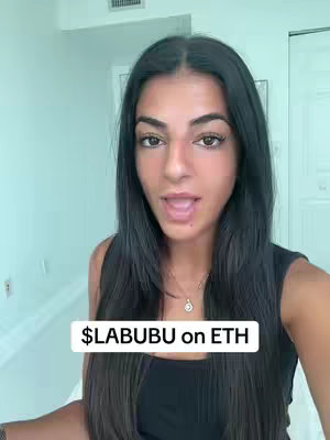 A young woman with long dark hair and a tank top speaks into the camera. A banner with white block letters stating $LABUBU on ETH is positioned at the bottom of the image. The background is an interior with a wall and a doorway visible.