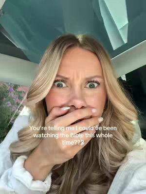 A woman with long blonde hair is shown close-up, she has wide eyes and her mouth covered by her hand with a concerned expression. The background includes a car's interior and exterior.