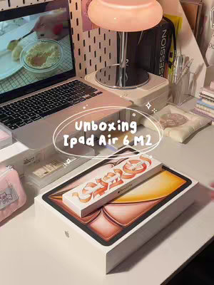 The cover image is a top-down shot of a desk with a laptop, an iPad box, and an Apple Pencil box. The iPad box is open, revealing the device inside. In the background, there is a lamp, pens, and other desk items.