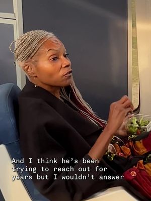 An African-American woman with blonde braids sits on a blue seat, holding a container with a salad. The background has a dark panel and a train window.