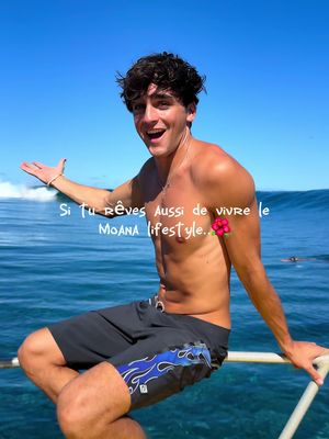 A young man with dark curly hair smiles broadly, leaning slightly to his right. He's shirtless, wearing dark blue swim trunks, and sitting on the edge of a boat with a blue ocean and sky in the background. Text overlays the image, and a tropical flower is added near the man's chest.