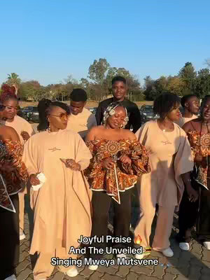A group of people, mostly women, dressed in similar beige outfits, smiling and looking toward the camera. They are standing outside under a bright sky. Text overlays the image.