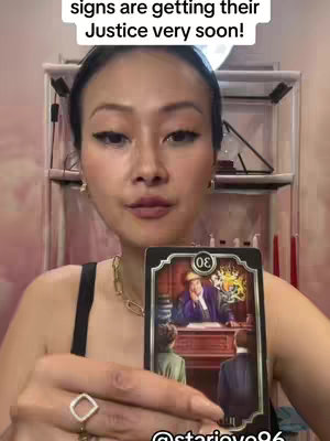 A woman with long dark hair is holding up a tarot card. The top of the image has white text. The background is blurry.