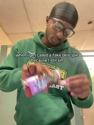 A young Black man in a green hoodie pours a purple liquid from a small bottle into a medicine cup. Text overlayed on the image reads "when I get called a fake desciple because I still sin."