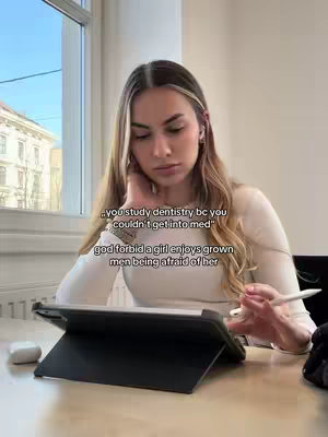 A young woman with long blonde hair is seated indoors near a window. She is holding a tablet with a stylus, appearing to be writing or drawing. Text overlays are placed on the image.