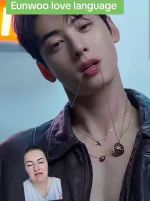 The image shows a close-up shot of a man, presumably Eunwoo. He is positioned slightly off-center, looking towards the camera. A text overlay at the top reads, 'Eunwoo love language'. The man has dark hair and is wearing a dark leather jacket. He has multiple necklaces. In the bottom left corner, there is a smaller inset image of a woman making a distressed face.