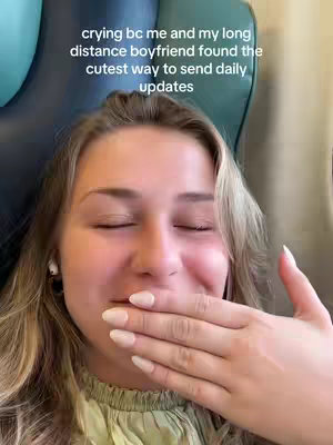 A close-up shot of a young woman with long blonde hair and fair skin, covering her mouth with her hand as if she is trying not to cry. The background suggests the interior of a car with a green seat cover and blue headrest.