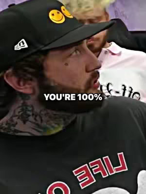 A man with a tattoo on his neck wearing a black hat with a smiley face on it and a black shirt that says "LIFE" in red.
