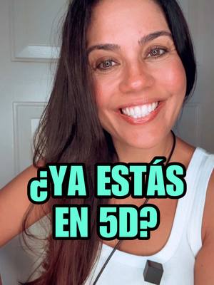 A woman with dark hair and brown eyes smiles directly at the camera. A superimposed text, '¿YA ESTÁS EN 5D?' in a blue-green, bubble-letter font, is placed over her chest. She wears a white tank top and a black necklace. The background is a light colored wall with a door on the left side.