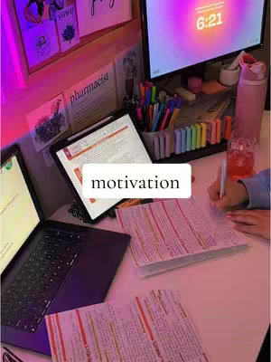 A desk setup with a laptop, tablet, and monitor, illuminated by a pink and purple glow. Papers and study materials are scattered around, with a hand writing in a notebook. The word 'motivation' is overlaid on the image.