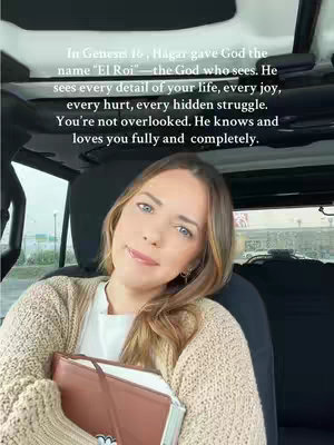 A woman with light brown hair is seen from the chest up, seated inside a vehicle. She is wearing a cream-colored sweater over a white shirt and holding a closed brown book near her chest. Text is overlaid at the top of the image, while the background is blurred.