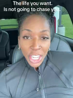 A close-up shot of a woman speaking directly to the camera, seated in a car. She has dark hair pulled back and wears large hoop earrings and a black jacket. Text overlays are present at the top.