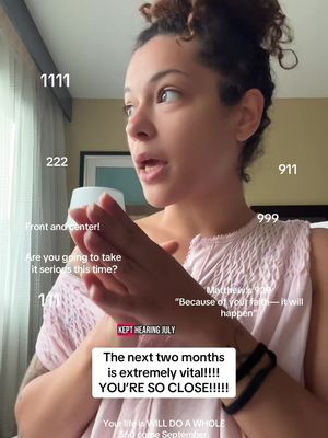 A young woman with dark hair and a white top looks to the side, gesturing with her hands, with superimposed text and numbers. The background features curtains and a blurred image.