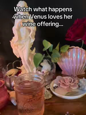 The cover image showcases a setup with elements related to spirituality and possibly witchcraft. In the center, a clear glass jar contains a pink liquid. To the jar's left is a white statue, with its arms extended. A variety of items, including a pink seashell-shaped object and a small white stone, are placed around the central jar, all set against a dark background. The overall composition evokes a sense of mystical practice and reverence.