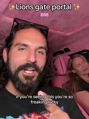 A selfie-style shot inside a car with a man in the foreground and a woman in the background. The man is speaking, the car has pink upholstery, and text overlays add context.