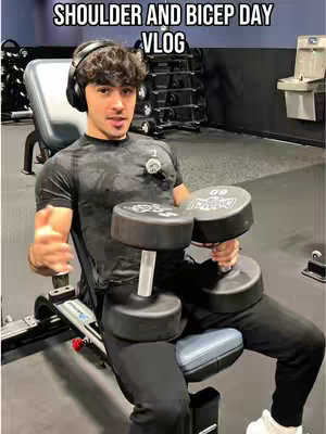 A person is seated on a workout bench, holding two dumbbells. Text overlay indicates the video's content. The setting appears to be a gym.