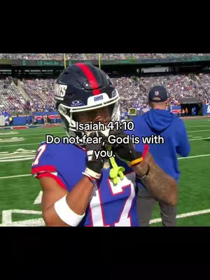 A football player in a Giants uniform is seen on a football field, with overlayed text. The player is facing the camera, wearing a helmet and holding the chin strap. In the background, a coach is visible, and the stands of the stadium are filled with spectators.