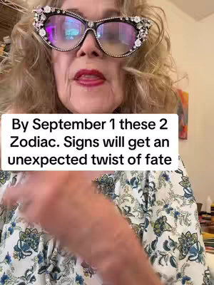 A woman with curly blonde hair is the central figure in the frame. She wears oversized, decorative glasses with clear lenses, styled with jewels. Her lips are slightly parted, and she seems to be speaking. She wears a patterned top, and a text overlay occupies the lower part of the frame.