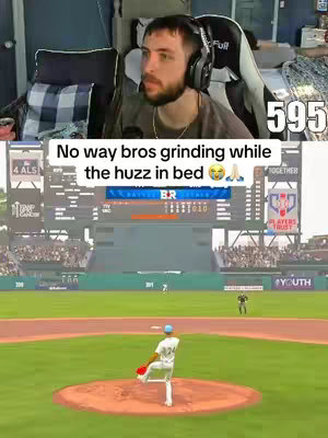 The image is a split-screen. The top half shows a person in a gaming chair with headphones on, the background behind this person is a dark room, and a digital counter with the number "595" is on the top right. The bottom half shows a screen capture of a baseball video game, with a baseball field. The text overlay in the image reads "No way bros grinding while the huzz in bed" with emojis.