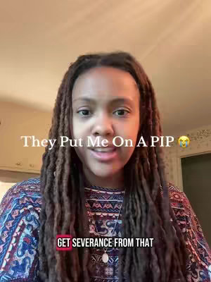 A young Black woman with long braided hair is centered in a selfie-style video. She is wearing a patterned top and a necklace. Text overlays are present, and she is smiling slightly.