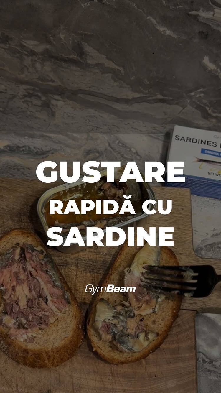 The image shows a close-up shot of a food spread. Two slices of bread are topped with a sardine mixture, with a fork on the side. In the background, there is a can of sardines partially visible, and a marble-like surface.