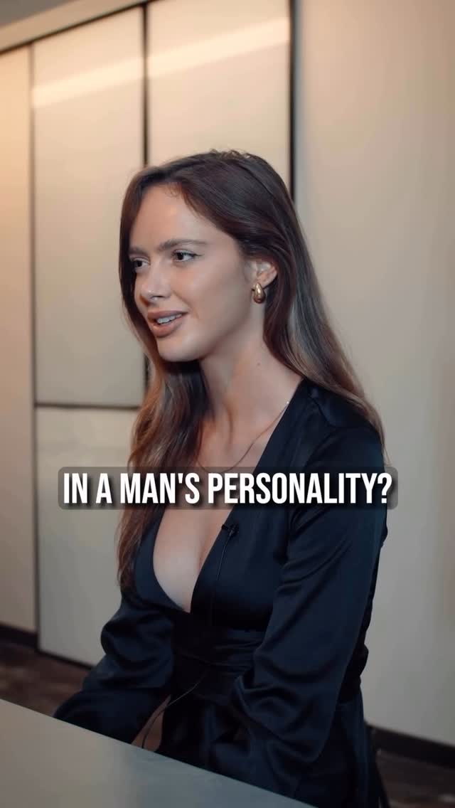 A woman is seated in front of a backdrop with neutral tones. The woman is wearing a black dress and gold earrings. Text overlay reads "IN A MAN'S PERSONALITY?"