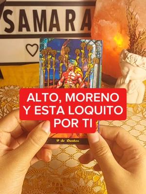 A person's hands hold a tarot card, the card is in focus and has imagery of a person holding up nine staffs with a man in the centre. A red text box with the text: "ALTO, MORENO Y ESTA LOQUITO POR TI". The background is a textured golden tablecloth and a decorative box with the word SAMARA and a heart shape.