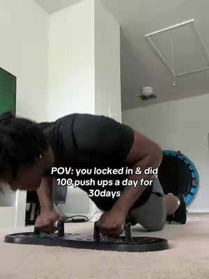 A man is performing push-ups on a push-up board in a room with a white ceiling, and a dark green television on the wall. The image is well-lit.