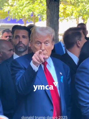 The image features Donald Trump, the primary subject, pointing directly at the viewer suggesting engagement or a call to action. He is surrounded by a group of people, all appearing in suits and ties, implying some formal setting or event. The background is somewhat blurred but gives the impression of an outdoor location or possibly a building facade with a touch of greenery. The color palette is dominated by rich blues and reds—Trump's suit, red tie, and the overall lighting suggest a scene of importance. At the bottom of the frame the text overlay says "donald trump dance 2025", while the "ymca" logo is positioned at the lower middle of the frame.