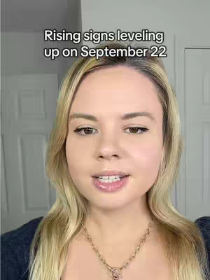 A woman with blonde hair and a gold necklace looks into the camera. Above her is text that says 'Rising signs leveling up on September 22'. The background is a white door. The lighting gives a moderately bright exposure.