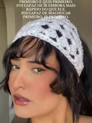 A close-up selfie of a woman with medium-length black hair and a white crocheted headband. Her skin appears smooth with blush applied to her cheeks. She's looking slightly off-camera, and her lips are glossy. The background is blurred out.