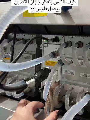 A close-up shot of a machine with many tubes and cables, likely a medical device. The image is slightly out of focus, concentrating on the interior parts of the machine, along with a hand that appears to be touching it.