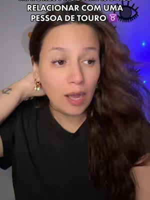 A woman with long brown hair looks directly at the camera, speaking with an open mouth. She wears a black top and small earrings. The background includes what appears to be a room with blue lighting. Text is overlaid at the top of the frame.