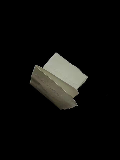 A cover image with a black background and a three-dimensional, abstract form in the center. This form appears to be folded or crumpled paper, with torn edges suggesting a tactile texture. The paper has a light gray or off-white color.