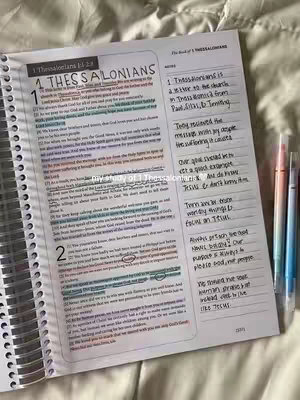 An open Bible rests on a neutral surface, revealing a detailed spread from the book of 1 Thessalonians. Handwritten notes fill the margins, and colorful highlighters mark the text, suggesting a study session. The layout is clean and inviting.