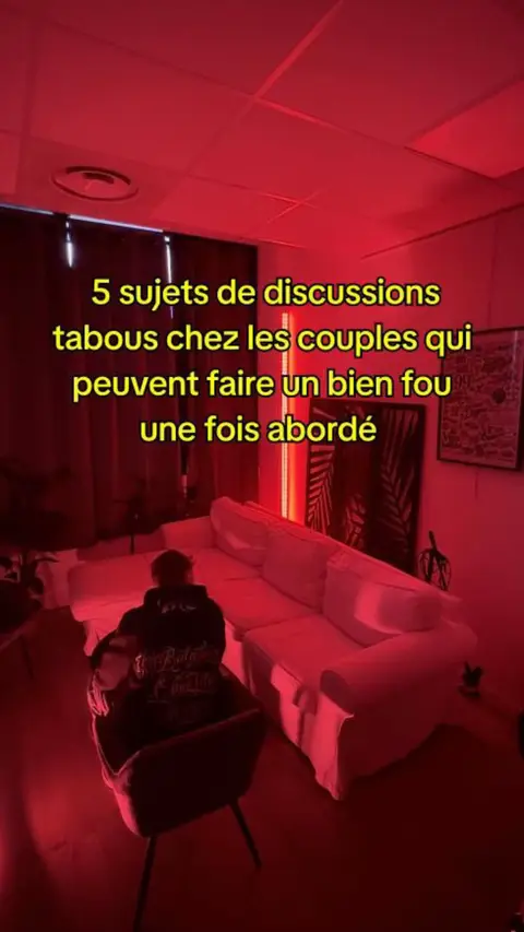 The cover image shows a room bathed in red light. A person wearing a hoodie is sitting in a chair with their back to the camera. A white sofa is visible. Text overlays indicate the video's topic is about discussions for couples.