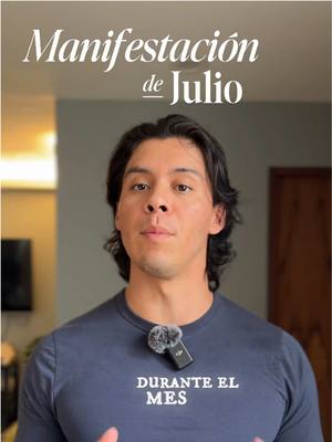 A man stands in front of a blurred background, the title of the presentation over his head says, Manifestacion de Julio'. He has dark hair and a microphone attached to his shirt. Text on his shirt reads 'DURANTE EL MES'.