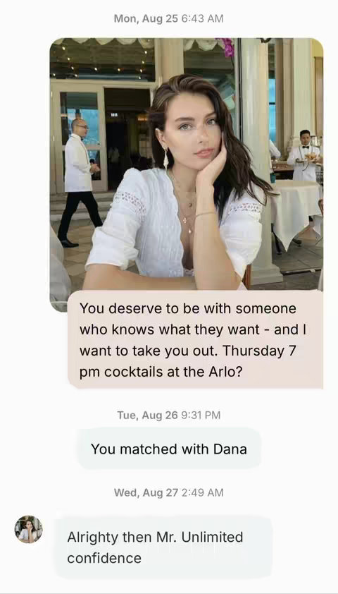 A selfie-style photo in a restaurant setting. A woman with brown hair, wearing a white top, is seated, with her hand near her chin. A text message conversation is overlaid on the image, with bubble-style text. Two waiters in white shirts and black pants are in the Background.
