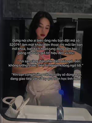A selfie taken in a well-lit bathroom. The woman is facing the mirror, with text overlays describing a numerical code for attracting money. The background features a bathroom sink with a silver faucet and a towel and toiletries in the background.