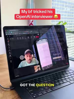 A man is on a video call displayed on a laptop screen. A phone is leaning against the screen, also displaying text. Above the laptop screen, a red bar reads, "My bf tricked his OpenAI interviewer 😂." Below on screen, it reads, "GOT THE QUESTION."
