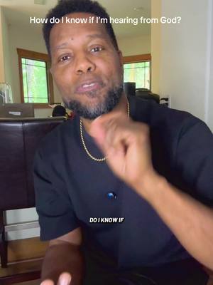 A man is filmed in a home setting, pointing while speaking. Above him is overlaid text asking, "How do I know if I'm hearing from God?" The image is lit with natural light from a window in the background.