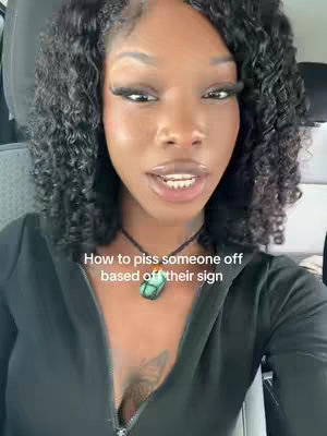 A selfie-style video features a fair-skinned Black woman with long, curly black hair. She wears a black top with a prominent necklace featuring a teal pendant. The text overlay reads: "How to piss someone off based off their sign". The background subtly suggests a car interior.