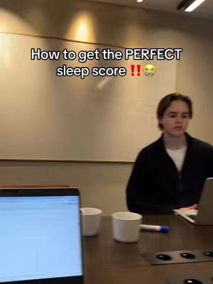 A person is sitting at a table with a laptop and two cups. The background is a white board in a bright room. Text that says How to get the PERFECT sleep score !! is added as a hook on the image.
