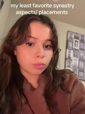 A young woman with long dark hair is looking at the camera, the text overlay says what her least favorite synastry is. Behind her are blurred objects.